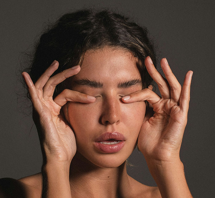 Young woman with closed eyes using fingers to press her eyelids, symbolizing frustration after catching ex cheating.