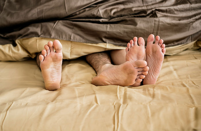 Two pairs of bare feet sticking out from under a blanket on a bed, related to catching cheating on Spotify.