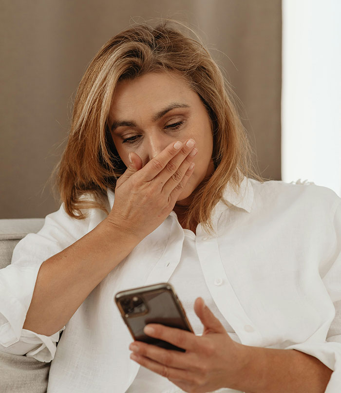 Woman in white shirt looking shocked while checking her smartphone, relating to catching cheating on Spotify.
