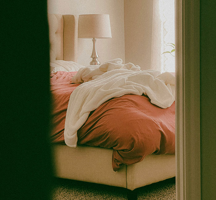 Messy bedroom with rumpled sheets and a lamp, illustrating stories about weird ways people caught their exes cheating.