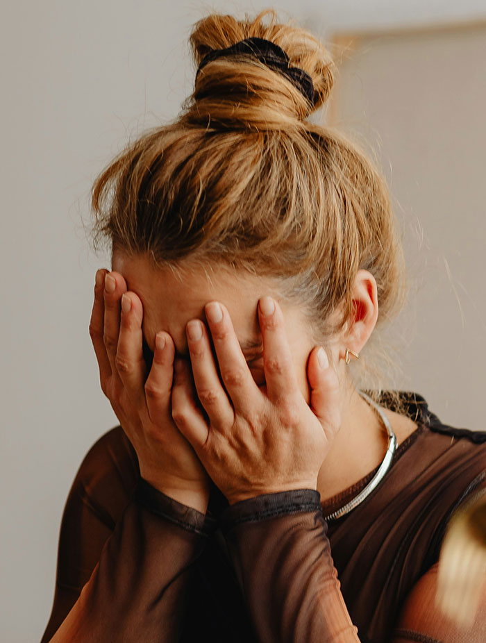 Woman covering her face with hands, expressing shock and sadness related to catching an ex cheating on Spotify playlist.