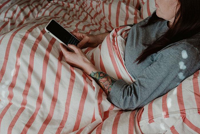 Person lying in bed with tattooed arm using smartphone, representing weird ways people caught their exes cheating.