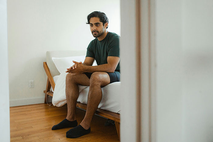 Man sitting on the edge of a bed looking thoughtful, illustrating stories about catching exes cheating through Spotify clues.