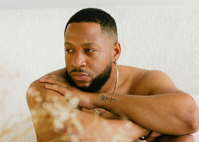 Man with tattoo and earring looks thoughtful and reflective while resting arms, illustrating stories about catching ex cheating on Spotify.