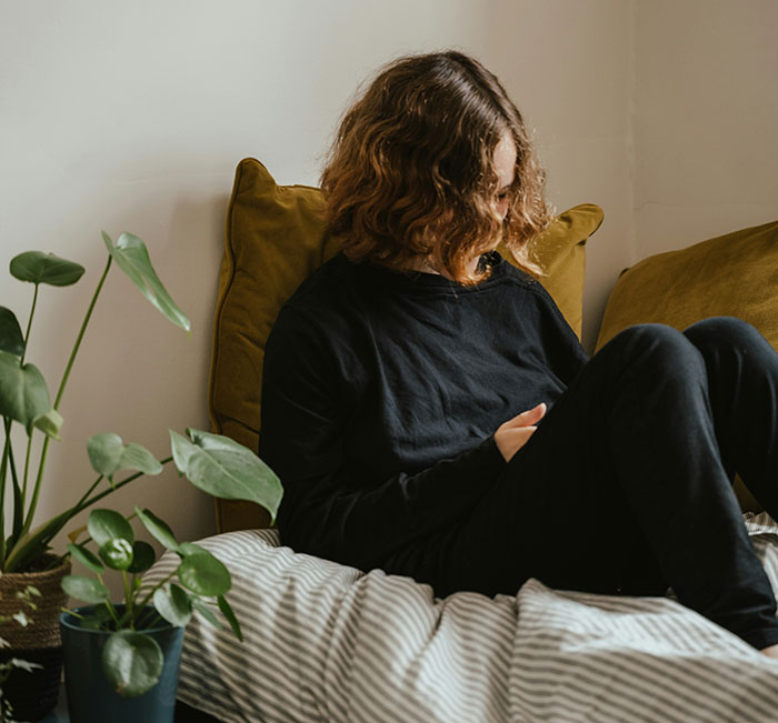 Person sitting on bed looking at phone, illustrating stories about catching exes cheating through Their Spotify accounts.
