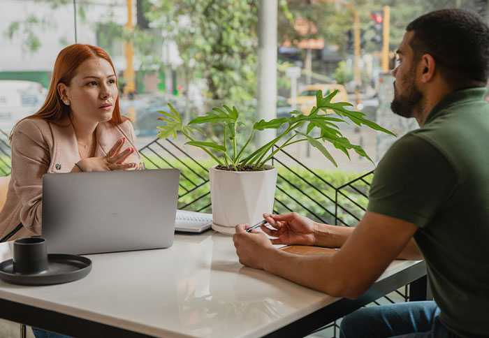 Two people engaged in a deep conversation displaying intelligence in a bright cafe setting with a laptop nearby.