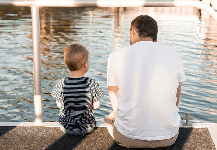 Man and young boy sitting by water, sharing a quiet moment reflecting on creepy displays of intelligence they've seen.