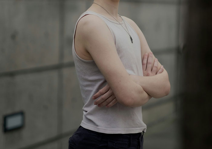 Person standing with arms crossed wearing a sleeveless shirt, portraying confidence and intelligence in a casual setting.
