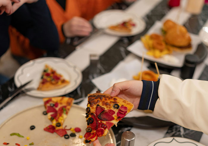 Hand holding a slice of pizza with olives and pepperoni, illustrating a casual moment of shared food and intelligence displays.