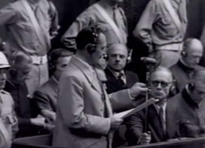 Black and white image of a man speaking in court, capturing a creepy display of intelligence witnessed by others.