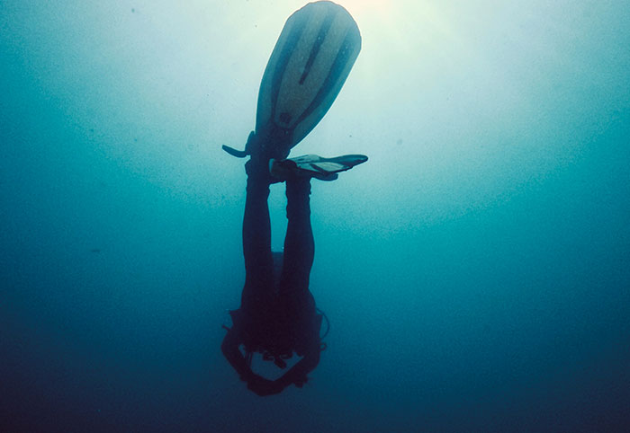 Scuba diver exploring deep dark ocean waters, highlighting some of the creepiest facts about the ocean below.