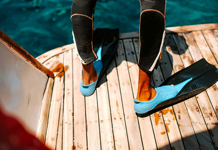 Person wearing blue fins and a wetsuit standing on a boat deck preparing to explore the ocean depths with creepy ocean facts.