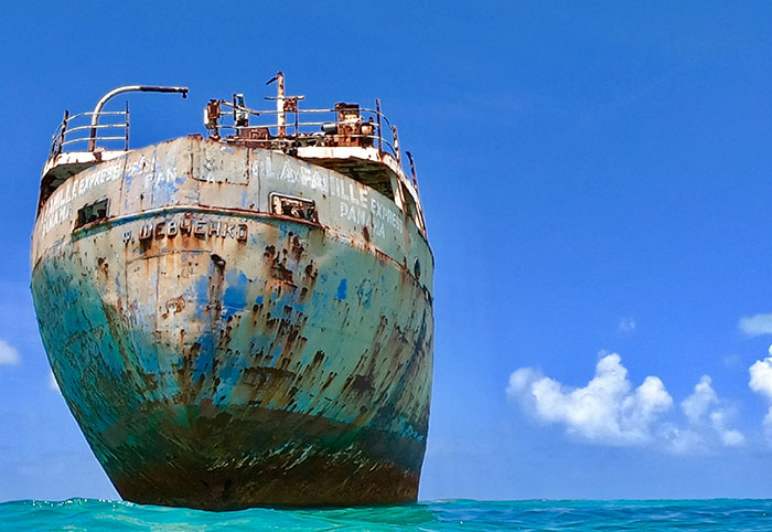 Rusty abandoned shipwreck floating on clear blue ocean water under a bright sky, highlighting creepy ocean facts.