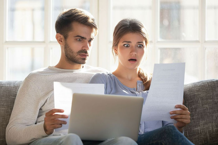 A man and woman shocked while reading vile letters on paper near a laptop, reflecting secret enemy vandalizing daughter's grave.