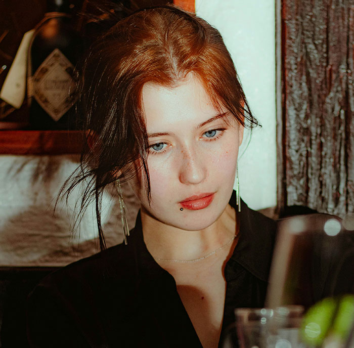 Young woman with piercing and red hair looking down, reflecting on stories of men hitting on women like absolute creeps.