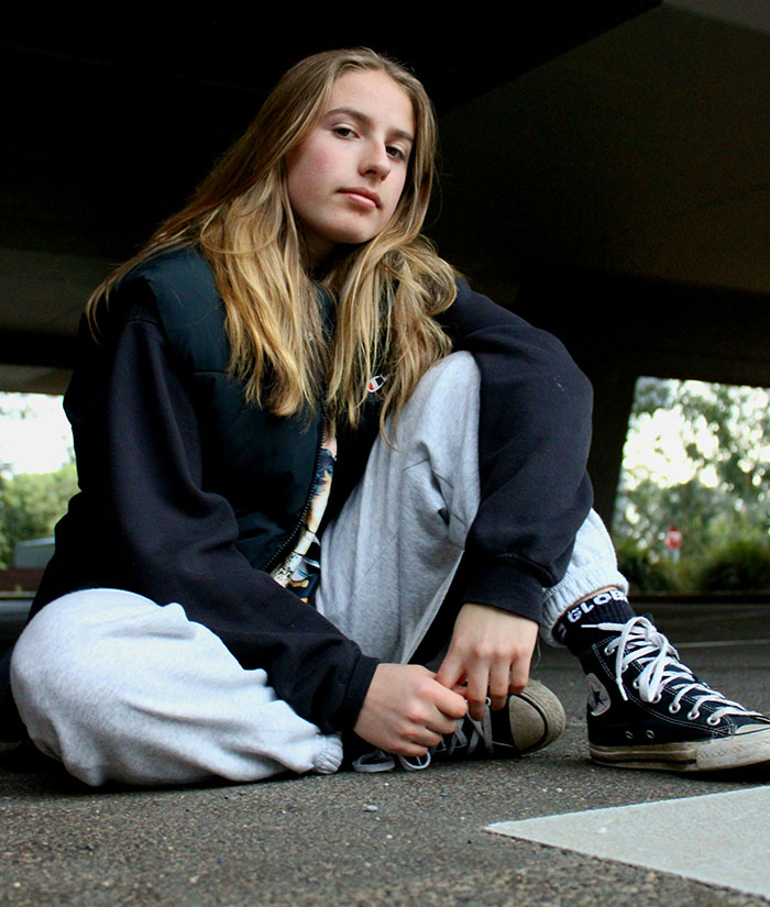 Young woman sitting on pavement under bridge, wearing casual clothes, reflecting on stories of men hitting on women like creeps.