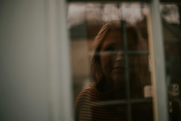 Woman looking through a window, reflecting on personal experiences of men hitting on them like absolute creeps.