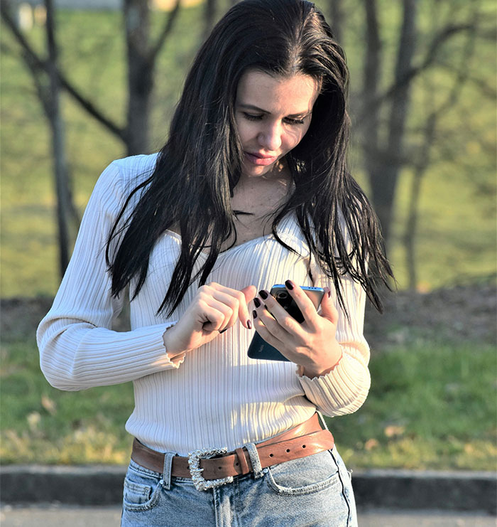 Young woman outdoors looking at phone, reflecting on enraging stories of men hitting on women like absolute creeps.