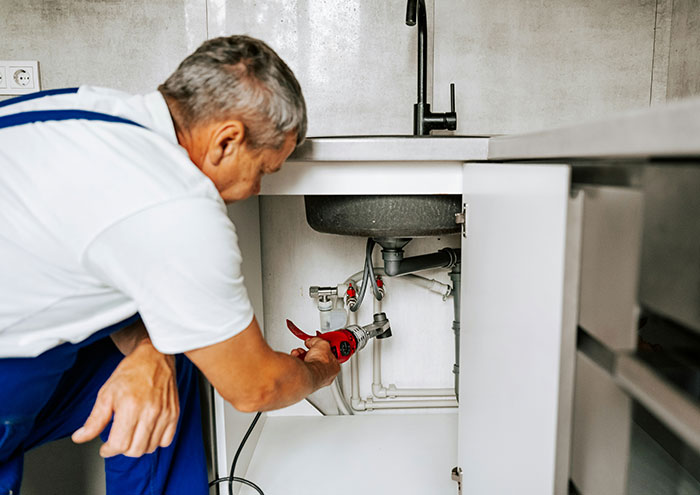 Man fixing pipes under kitchen sink, unrelated to stories of men hitting on women like absolute creeps.