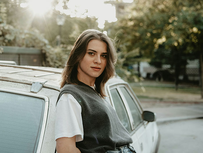 Young woman standing by a car outdoors, reflecting on enraging stories of men hitting on women like absolute creeps.