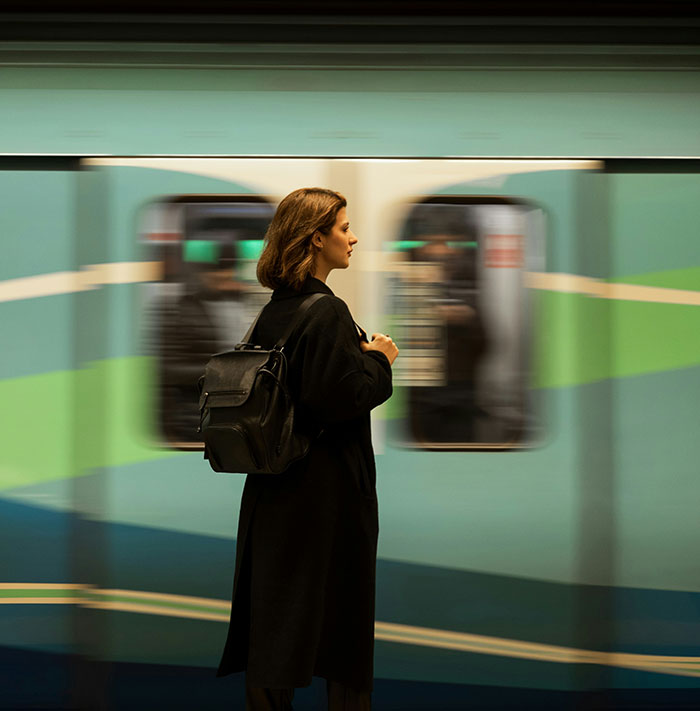 Woman standing on subway platform with backpack, portraying stories of men hitting on women like absolute creeps.