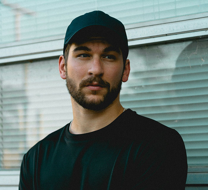 Young man in black cap and shirt posing outdoors, representing the theme of men hitting on women like creeps.