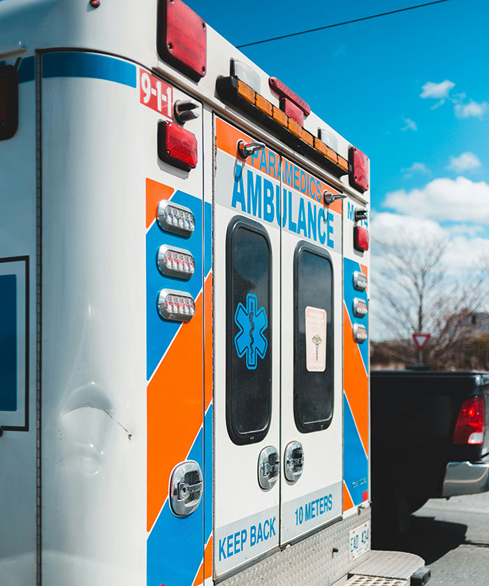 Ambulance parked under clear sky with paramedics signage, emergency lights, and 911 number visible on vehicle.