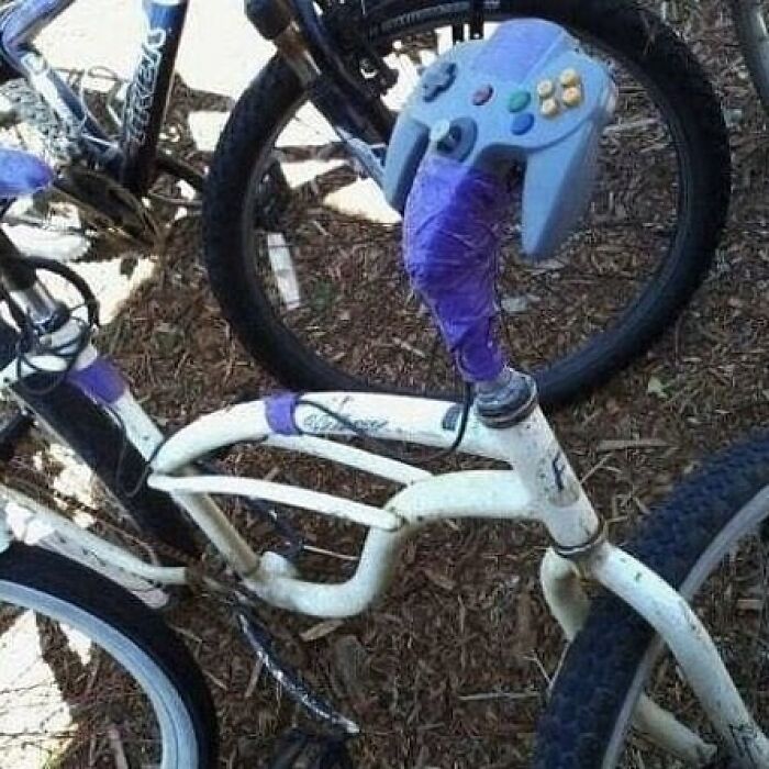 Bike handle wrapped with purple tape and a game controller used as an unusual bike grip, a weird and cringey photo.