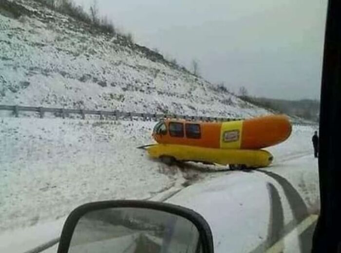 Weird and cringey vehicle shaped like a giant hot dog stuck in the snow by the roadside on a snowy day