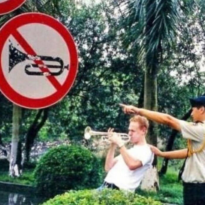 Man playing trumpet in front of no trumpet sign while being stopped by an officer in a weird and cringey photo