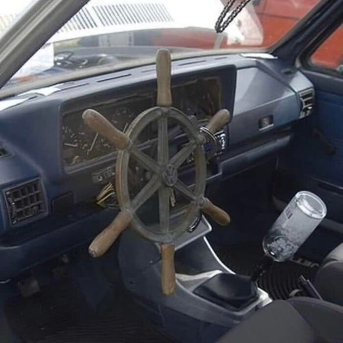 Car interior with a wooden ship steering wheel and a bottle used as a gear shift, showing weird and cringey design choices.