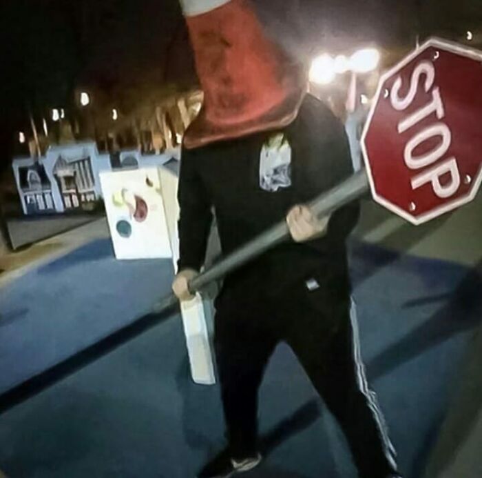 Person wearing an orange traffic cone on their head holding a stop sign awkwardly in a weird and cringey photo.