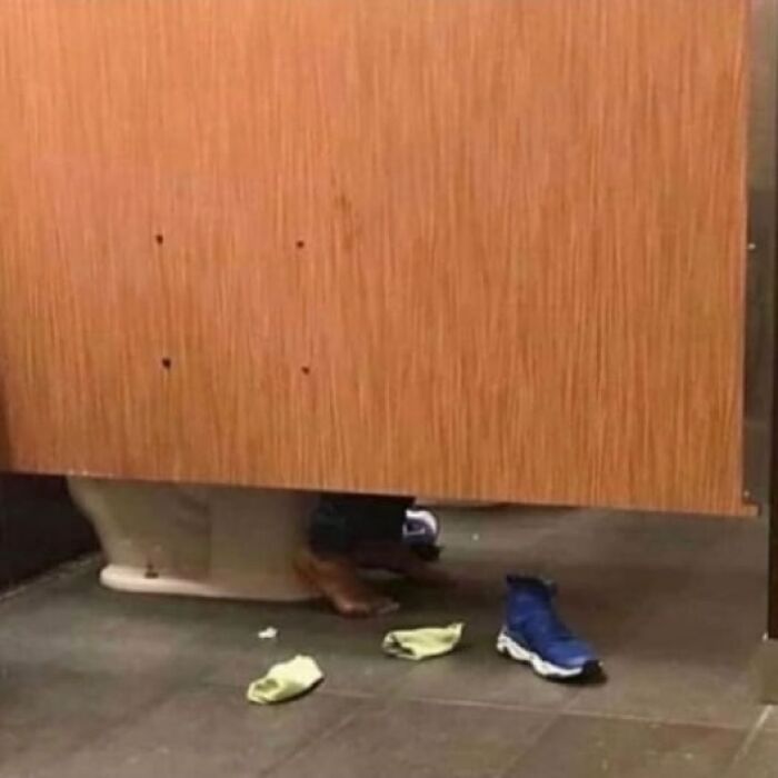 Feet visible under a bathroom stall with a shoe and socks on the floor, showing a weird and cringey photo moment.