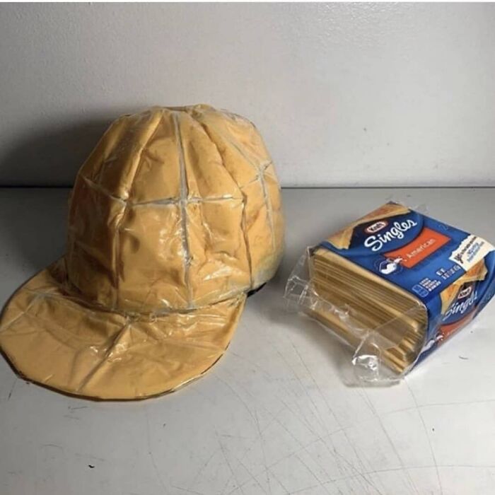 A melted cheese slice shaped like a baseball cap next to a pack of processed cheese slices, creating a weird and cringey photo.