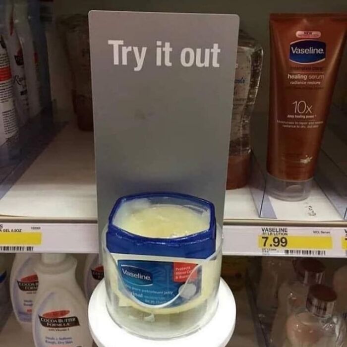 Open Vaseline container with a sign saying Try it out, displayed on a store shelf with other lotions.