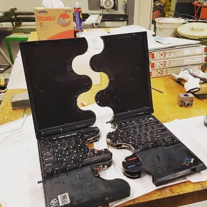 Broken laptop split into two puzzle-piece shaped halves on a workbench, a weird and cringey photo.