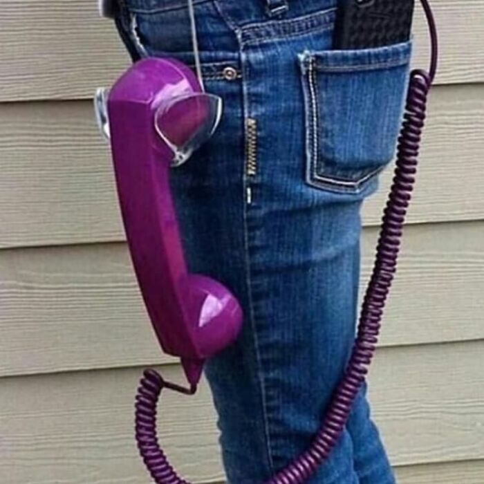 Old-fashioned purple phone handset awkwardly attached to a person's denim jeans, creating a weird and cringey visual.