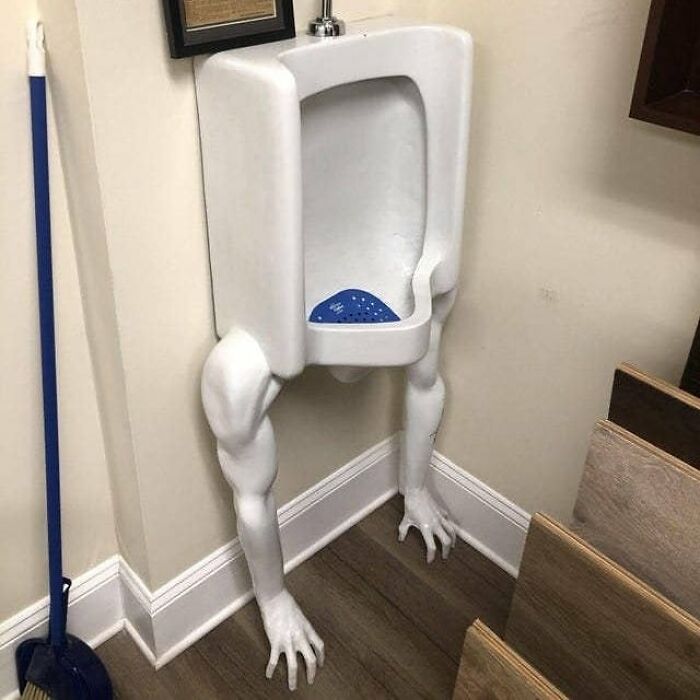Urinal with realistic muscular arms and hands replacing traditional legs in a bathroom corner, weird and cringey photo.