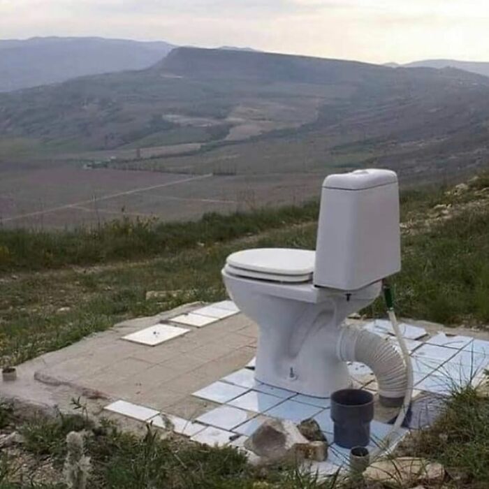 A toilet installed outdoors on a tiled platform in a rural area, showcasing a weird and cringey photo setup.