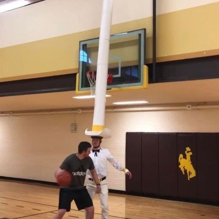 Two men playing basketball indoors, one wearing a tall, unusual hat, creating a weird and cringey photo moment.