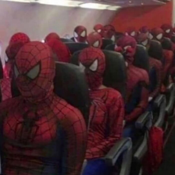 Multiple people wearing Spider-Man costumes sitting closely together on airplane seats, showcasing a weird and cringey scene.