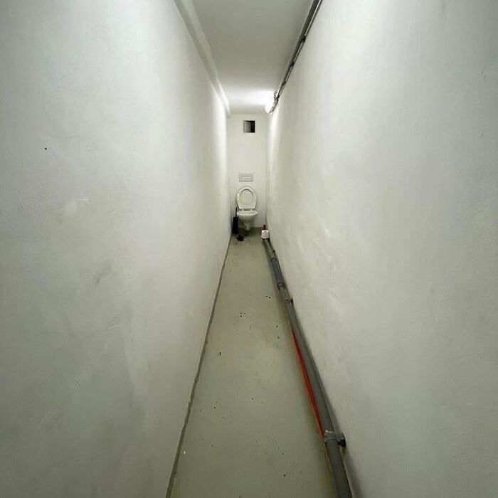 Narrow and awkwardly long bathroom corridor with a toilet at the far end creating a weird and cringey photo perspective.