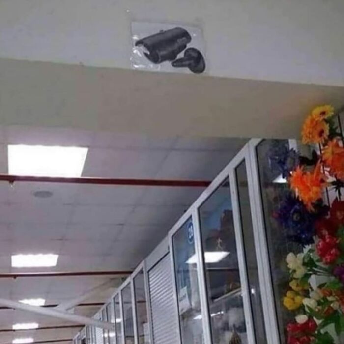 Fake security camera taped to a wall in a store interior, one of the weird and cringey photos difficult to look at