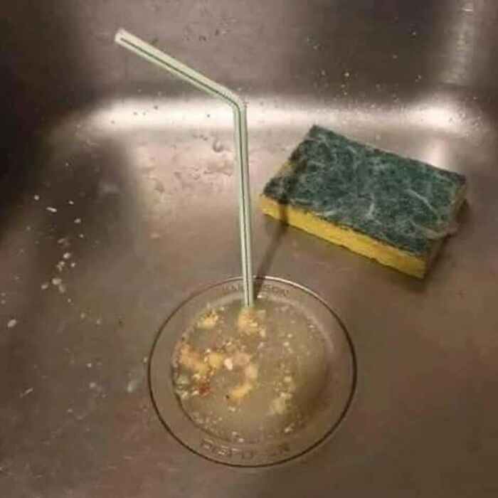 Dirty kitchen sink with food debris and a bent straw inserted in the drain, showing a weird and cringey photo.