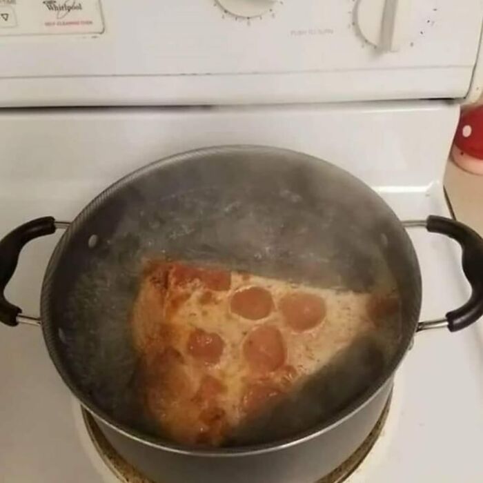 Slice of pepperoni pizza boiling in a pot of water on a stovetop, a weird and cringey food moment.