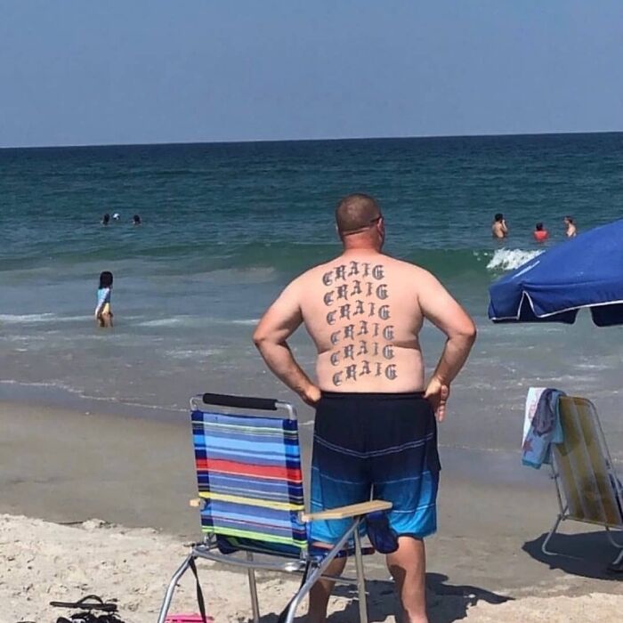Man at the beach with repeated tattoo of the name Craig on his back in a weird and cringey photo.