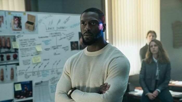 Man in a white sweater stands with arms crossed in an office, highlighting Prime Video&rsquo;s Cross success and renewal for season 3.