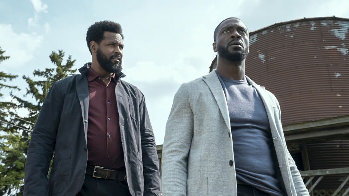 Two men standing outdoors near a rustic structure, representing Prime Video&rsquo;s Cross in a dramatic scene.