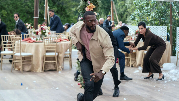Man in beige jacket running urgently during an outdoor event, highlighting Prime Video&rsquo;s Cross explosive streaming success.