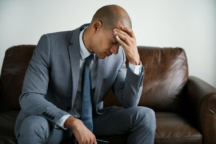 Man in gray suit sitting on a couch looking stressed and thoughtful, illustrating bizarre true stories disbelief.
